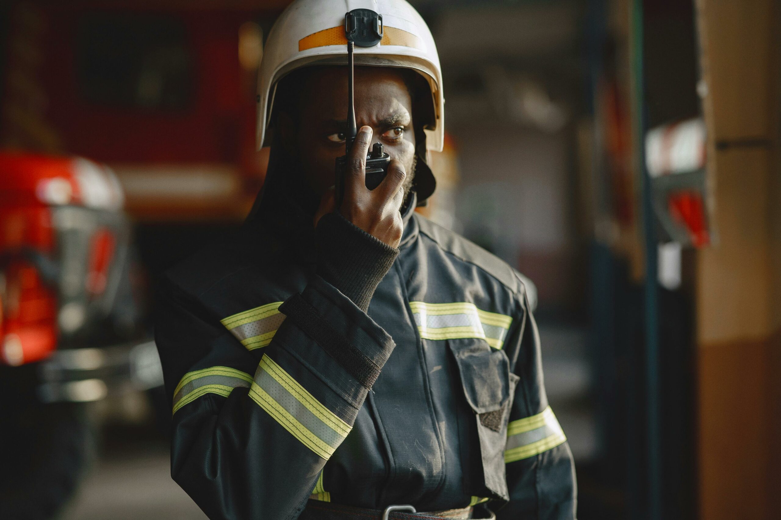 Close-up of a firefighter in uniform using a walkie talkie inside a fire station.